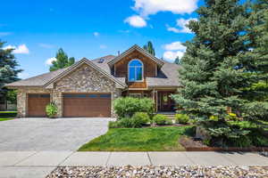 Craftsman inspired home featuring a shingled roof, decorative driveway, an attached garage, stone siding, and a front yard
