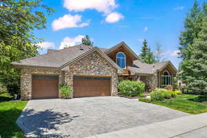 Craftsman-style home with stone siding, decorative driveway, and a shingled roof