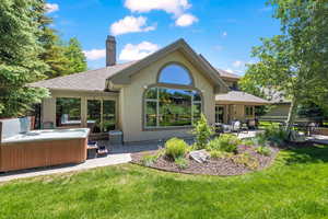 Rear view of house featuring a patio, stucco siding, a hot tub, a yard, and a chimney