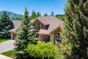 View of front facade featuring stone siding, decorative driveway, roof with shingles, an attached garage, and a mountain view