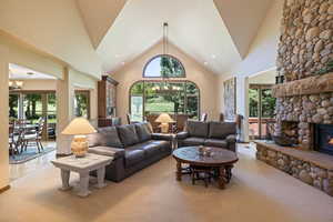 Living room with hanging lights, a high ceiling, carpet flooring, and a stone fireplace
