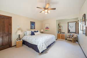 Bedroom with light colored carpet, a ceiling fan, and vaulted ceiling