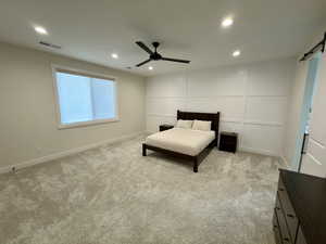 Bedroom with a barn door, a ceiling fan, recessed lighting, light colored carpet, and a decorative wall