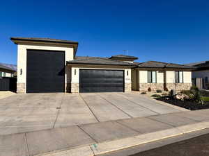 Prairie-style house featuring stucco siding, stone siding, a garage, and concrete driveway