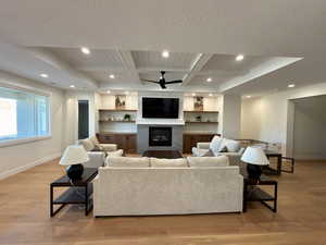 Living room with recessed lighting, light wood finished floors, coffered ceiling, a large fireplace, and ceiling fan
