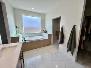 Bathroom featuring a garden tub, vanity, a walk in closet, and light marble finish flooring