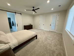 Bedroom featuring a barn door, light carpet, a ceiling fan, recessed lighting, and ensuite bath