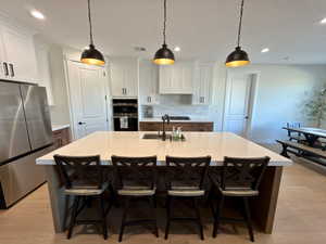 Two tone kitchen featuring stainless steel appliances, hanging light fixtures, a kitchen island with sink, two tone cabinets, and a kitchen bar