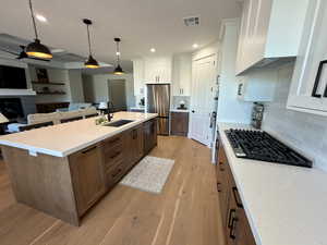 Two tone kitchen with decorative light fixtures, two tone cabinetry, light wood-style flooring, open floor plan, and light stone countertops