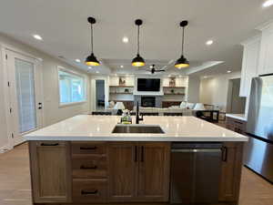 Dual tone kitchen with light wood-style flooring, open floor plan, stainless steel appliances, a glass covered fireplace, and a tray ceiling
