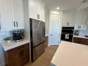 Dual tone kitchen with decorative backsplash, two tone color scheme, stainless steel appliances, light wood-type flooring, and light stone countertops