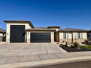 Prairie-style home featuring stucco siding, stone siding, an attached garage, and driveway