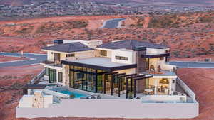 Rear view of house featuring a chimney, a patio, a balcony, stone siding, and a pool with connected hot tub