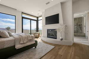 Bedroom with wood finished floors, a glass covered fireplace, access to outside, recessed lighting, and connected bathroom