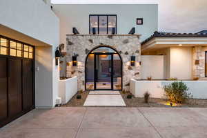 Entrance to property with stone siding, stucco siding, and a garage