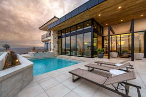 Pool at dusk featuring an outdoor pool, a balcony, and a patio area