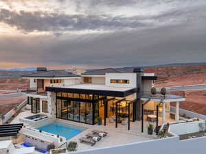 Back of property at dusk featuring a patio area, a chimney, a pool with connected hot tub, and a mountain view