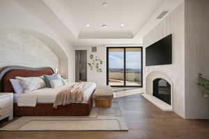 Bedroom featuring hardwood / wood-style flooring, access to outside, a tray ceiling, recessed lighting, and a large fireplace