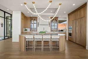 Kitchen with dark wood-type flooring, a kitchen island, glass fronted cabinets, a kitchen bar, and wood finish cabinetry