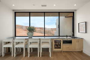 Bar area with wine cooler, stainless steel microwave, light wood-style floors, stone countertops, and recessed lighting
