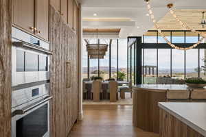 Kitchen with wood finish cabinetry, double oven, light wood-style flooring, floor to ceiling windows, and a mountain view