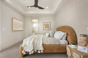 Carpeted bedroom featuring ensuite bathroom, a raised ceiling, a ceiling fan, and recessed lighting