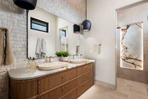 Bathroom with tiled shower, double vanity, and light tile patterned floors