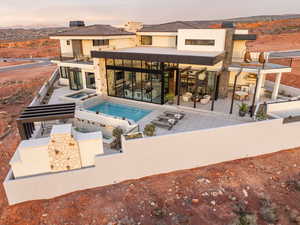 Back of house at dusk with a patio area, a mountain view, a pool with connected hot tub, stone siding, and a chimney