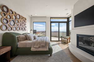 Bedroom with wood finished floors, expansive windows, a glass covered fireplace, access to exterior, and recessed lighting