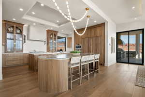 Kitchen featuring glass fronted cabinets, a breakfast bar, dark wood-type flooring, light stone countertops, and wood finish cabinets