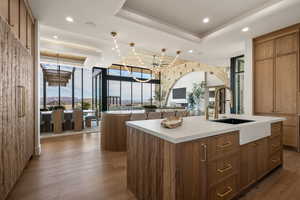 Kitchen with wood finish cabinets, a raised ceiling, an island with sink, floor to ceiling windows, and dark wood-type flooring