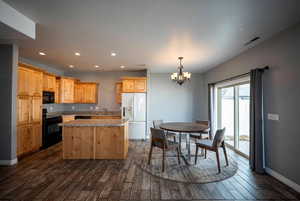 Kitchen featuring black appliances, hanging lights, a kitchen island, dark wood-style floors, and light wood finish cabinets