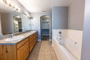 Full bath featuring a spacious closet, double vanity, a garden tub, light tile patterned flooring, and a textured ceiling