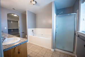 Bathroom featuring a walk in closet, vanity, a garden tub, a stall shower, and a textured ceiling