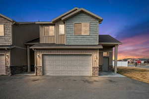 View of front facade with a garage, stone siding, asphalt driveway, and board and batten siding