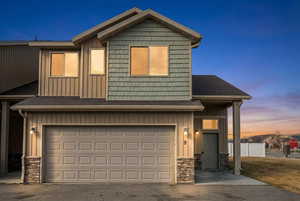 View of front of property featuring board and batten siding, stone siding, a garage, and a shingled roof