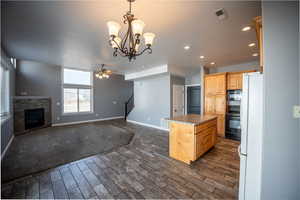 Kitchen featuring hanging lights, open floor plan, black appliances, wood tiled floors, and a center island