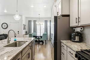 Kitchen with light wood finished floors, stainless steel appliances, pendant lighting, light stone counters, and white cabinets