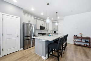 Kitchen with stainless steel appliances, a breakfast bar area, decorative light fixtures, a center island with sink, and light stone counters