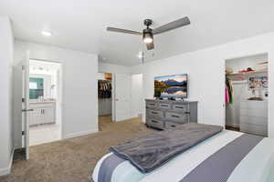 Bedroom featuring light colored carpet, a spacious closet, ceiling fan, and ensuite bathroom