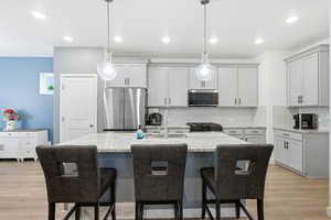 Kitchen with light stone counters, light wood-style floors, a kitchen bar, stainless steel appliances, and a kitchen island with sink
