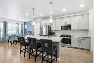 Kitchen featuring stainless steel appliances, light stone countertops, a kitchen island with sink, a kitchen breakfast bar, and light wood finished floors