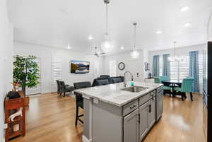 Kitchen featuring gray cabinets, light stone countertops, a center island with sink, and light wood finished floors