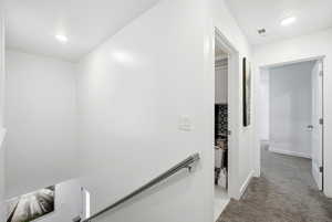 Hallway with light colored carpet and an upstairs landing