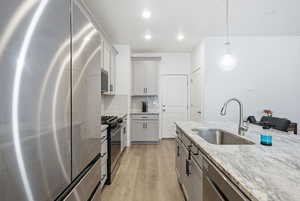 Kitchen featuring stainless steel appliances, decorative light fixtures, light wood-style flooring, light stone countertops, and backsplash