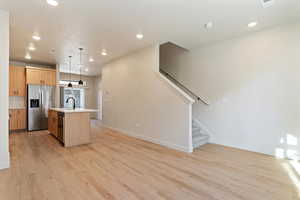 Kitchen with a center island with sink, light wood finish cabinetry, stainless steel appliances, and pendant lighting