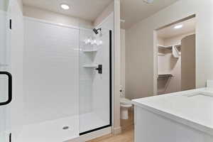 Full bath featuring vanity, a spacious closet, a shower stall, recessed lighting, and light wood-style floors