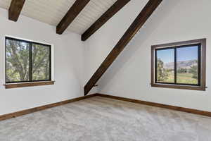 Empty room with lofted ceiling with beams, a mountain view, light colored carpet, plenty of natural light, and wooden ceiling