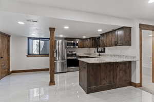 Kitchen with dark wood finish cabinets, stainless steel appliances, light stone countertops, a peninsula, and recessed lighting