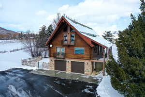 Log-style house featuring log siding, a garage, stone siding, a mountain view, and asphalt driveway